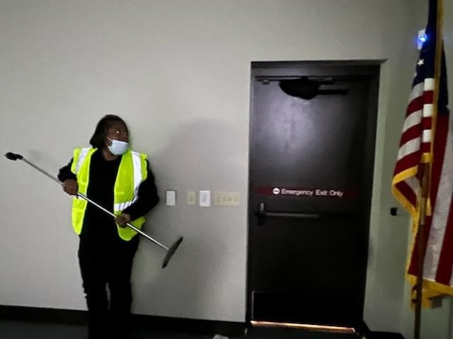A course participant holding a microphone stand stands against the wall as part of an active threat exercise during the Run. Hide. Fight. course.